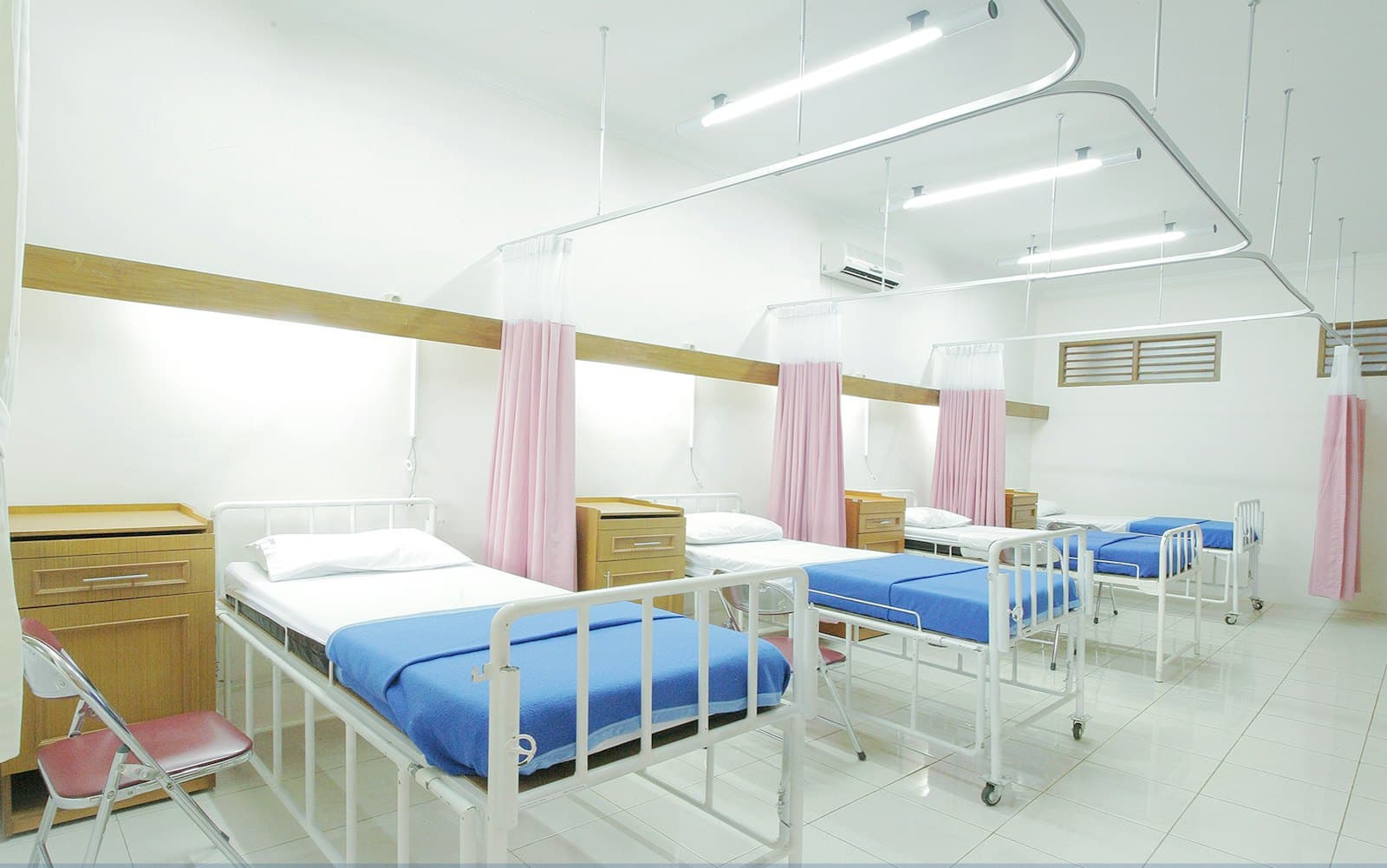 A bright inpatient ward with made beds and privacy curtains
